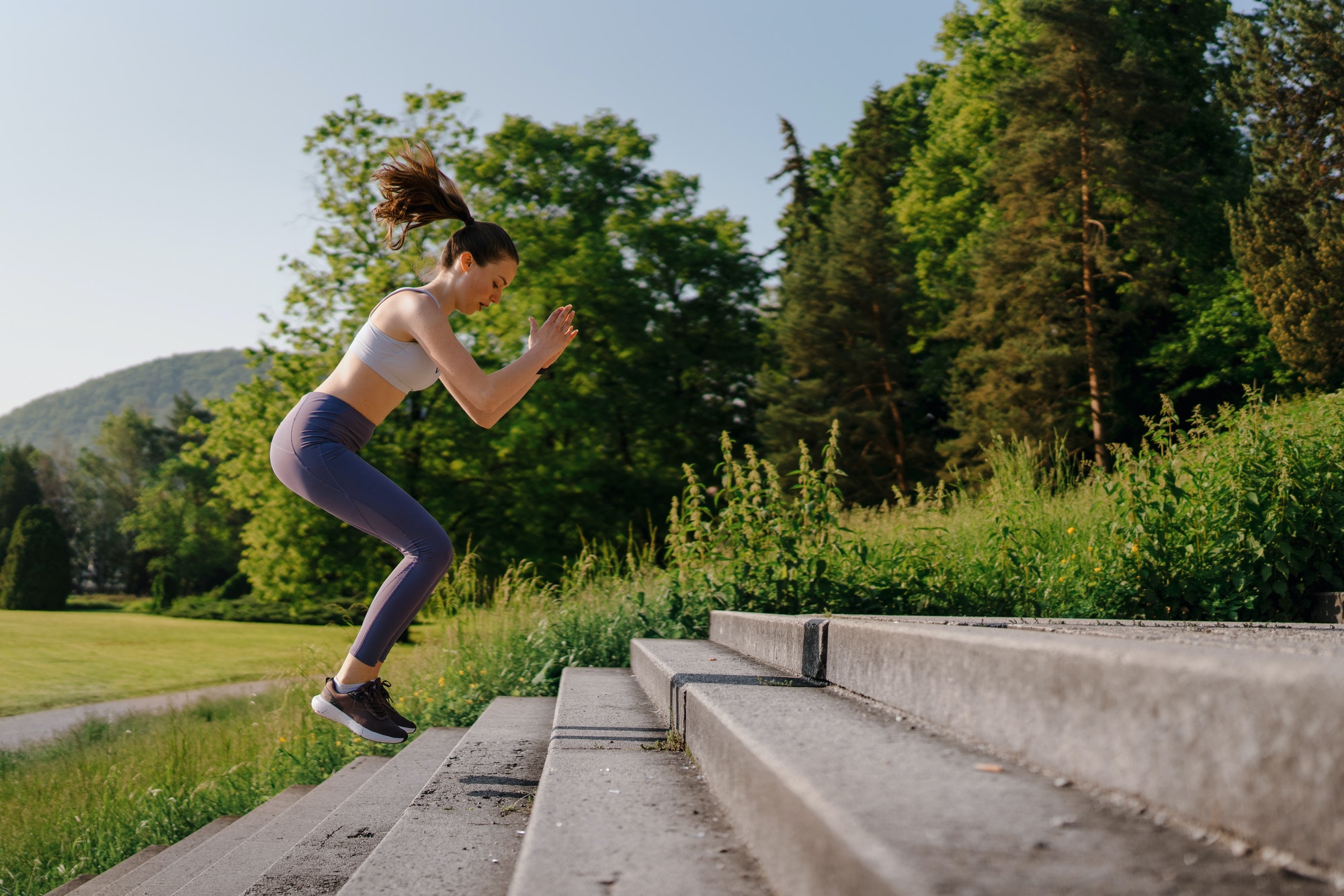 Sporty woman doing jumping squats exercise on stairs in city park.